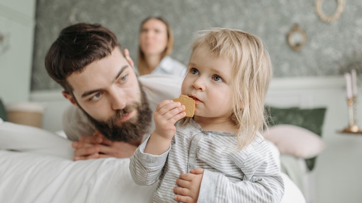 A loving father watches his baby daughter enjoying a snack at home. Warm and tender family moment.