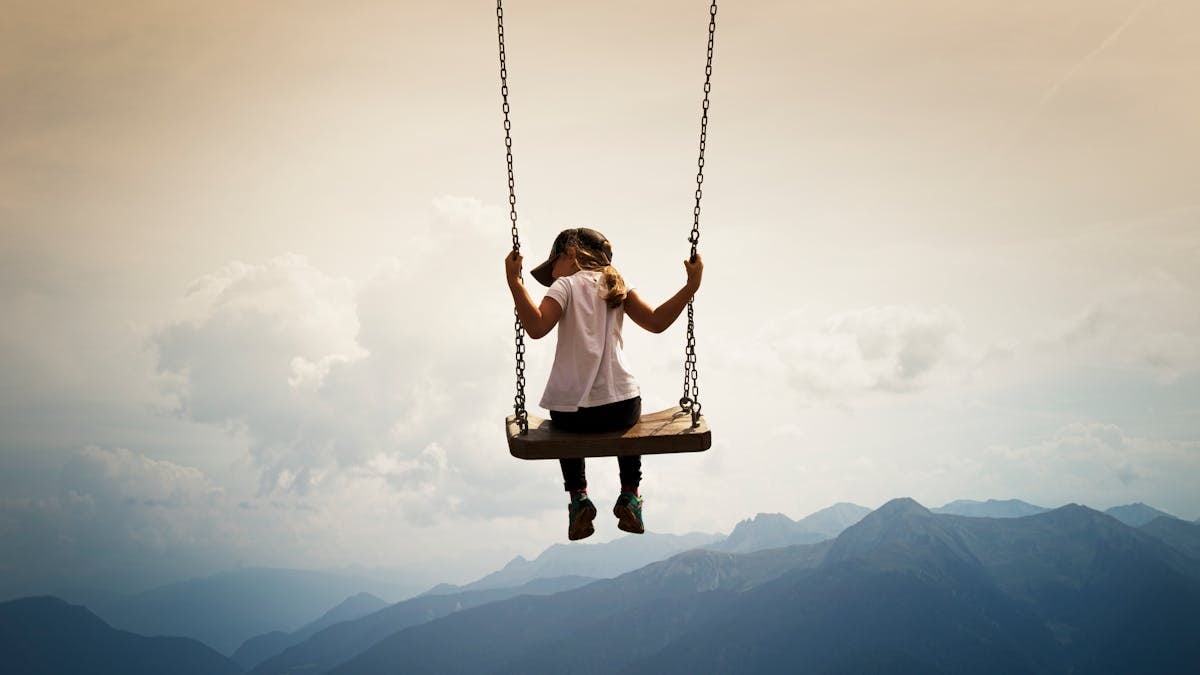 A girl swings high above the picturesque mountains of Vipiteno, Italy, embracing freedom and nature.